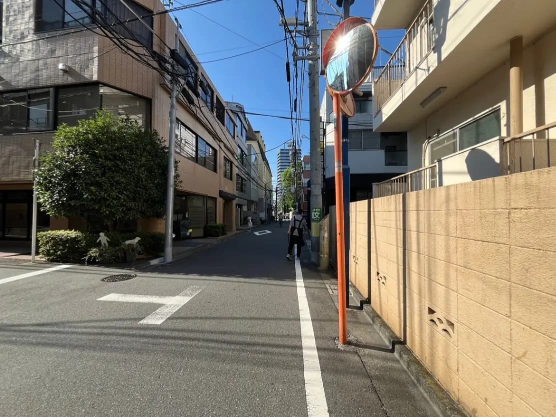 - 都会の静かな通り、青空の下に立つビルと緑の木、個性的なミラーが映る景色