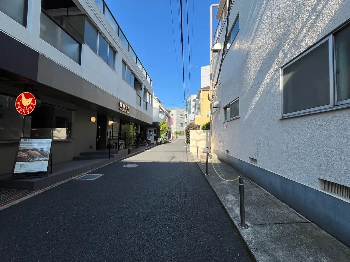 - 都市の街並みを背景にした、明るい青空の下の静かな道路、カフェと店舗の軒先が見える風景