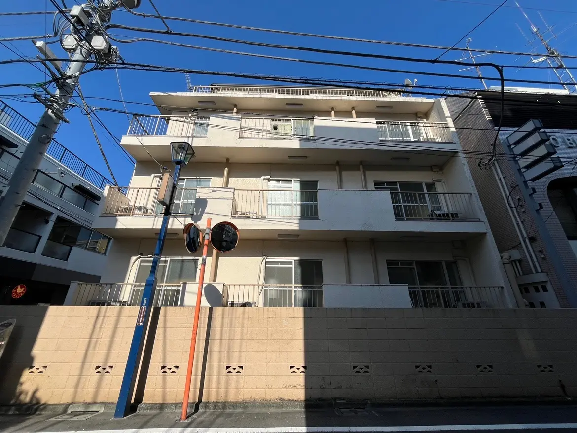 - 都市型アパートメントの外観、三階建てでバルコニーのある白い壁、晴れた青空と電線が見える場所