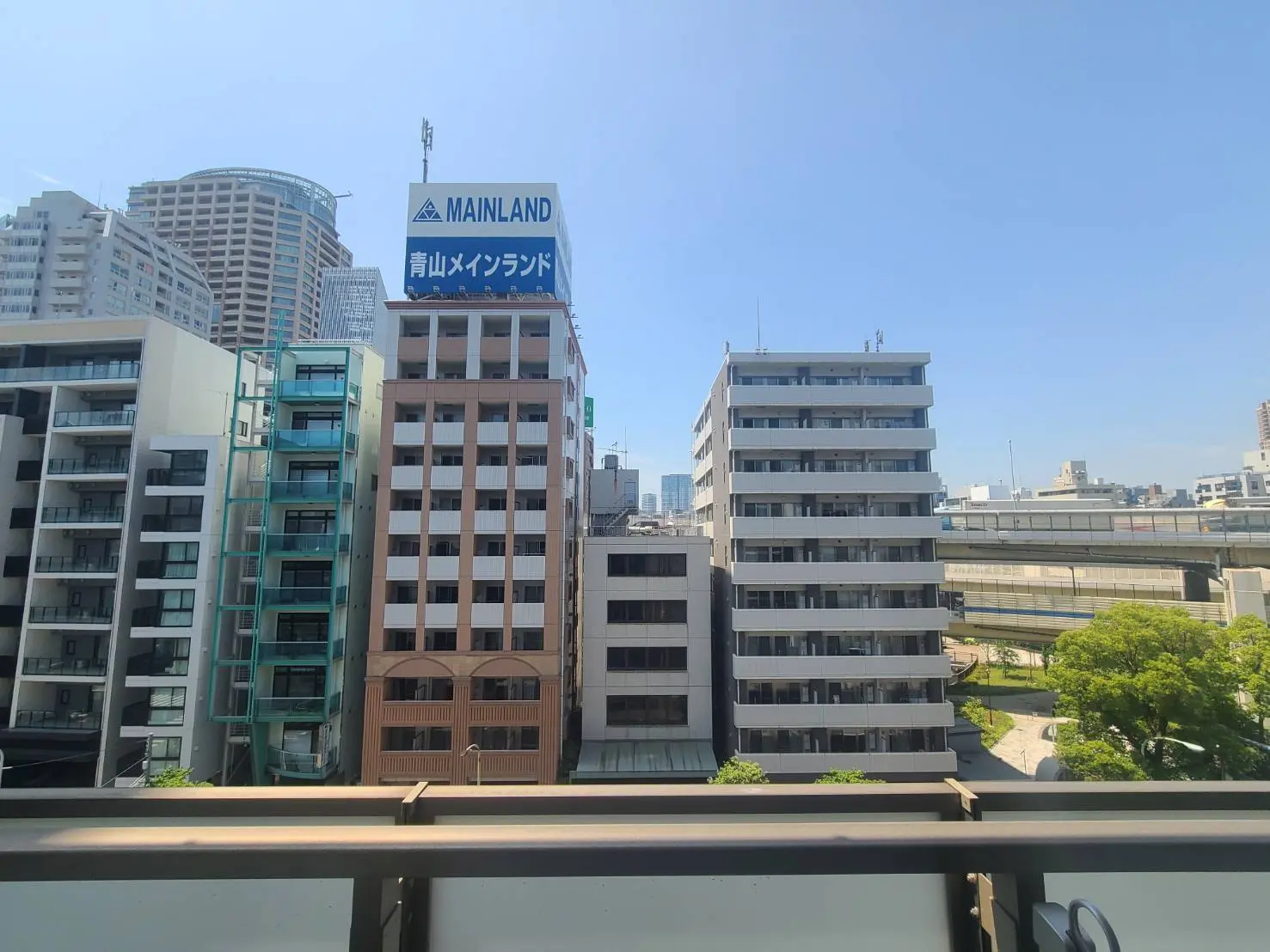 - 都市のビル群の眺め、青空と明るい日の光が映える中、高層ビルと低層ビルが立ち並ぶ風景