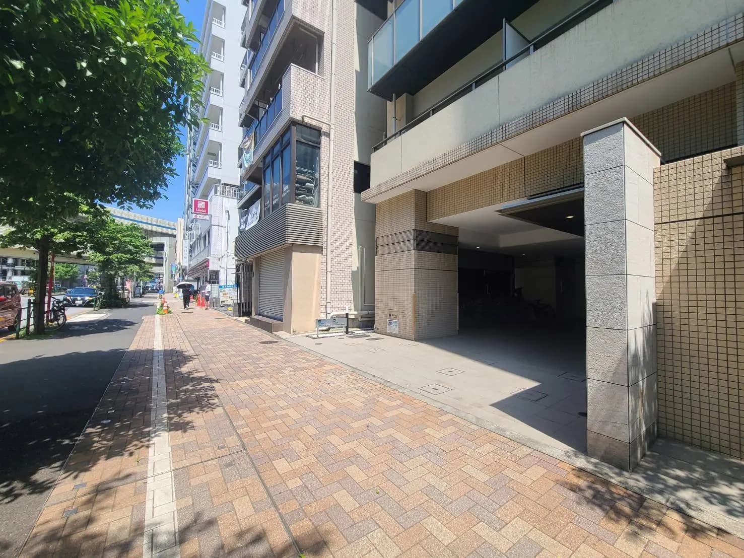 - 都市の商業エリアにある近代的なビルのエントランス、舗装された歩道と緑の木々が配された風景