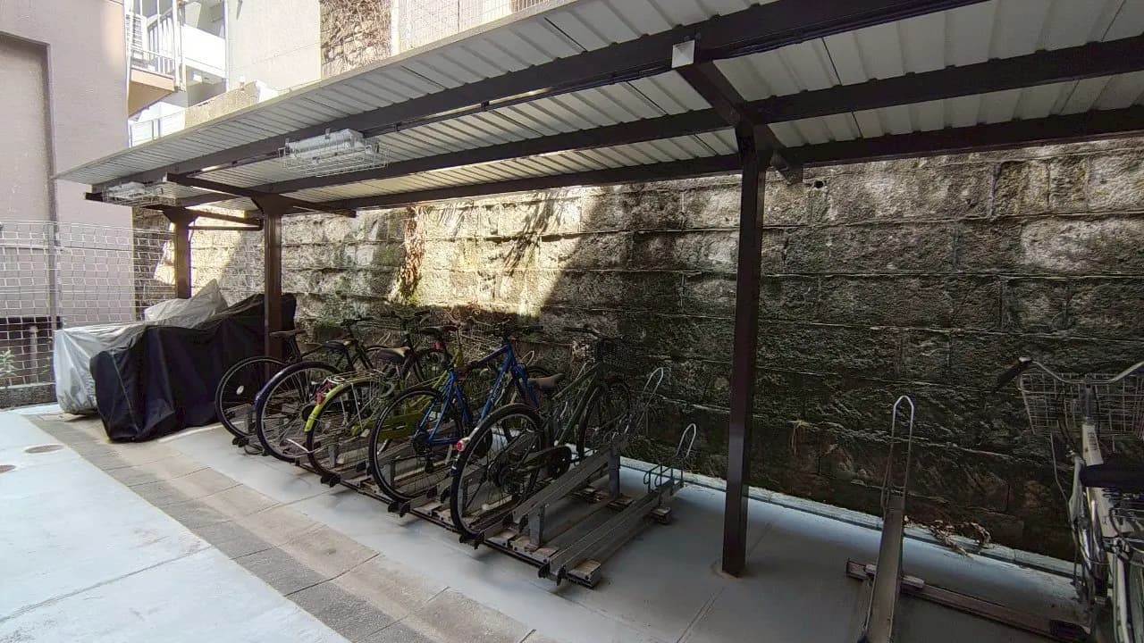 - 自転車置き場、屋根付きのスペースに並ぶ複数の自転車と石壁の背景