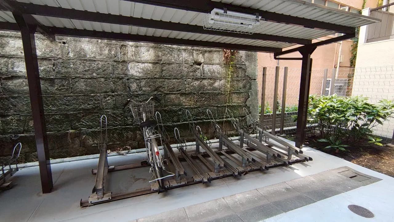 - 自転車用の屋根付き駐輪場、整然とした自転車ラックとコンクリートの床、背景には石壁が見える景観