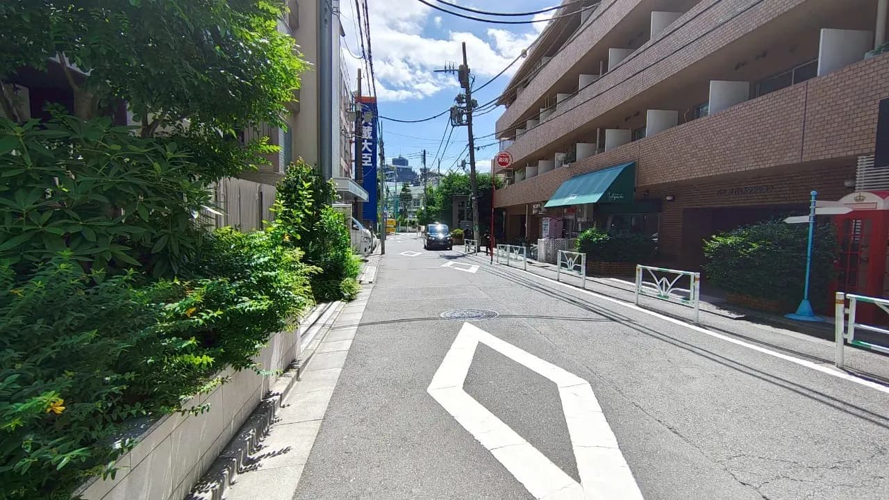 - 緑の植栽に囲まれた静かな路地、晴れた日に見える都市風景と建物が並ぶ様子