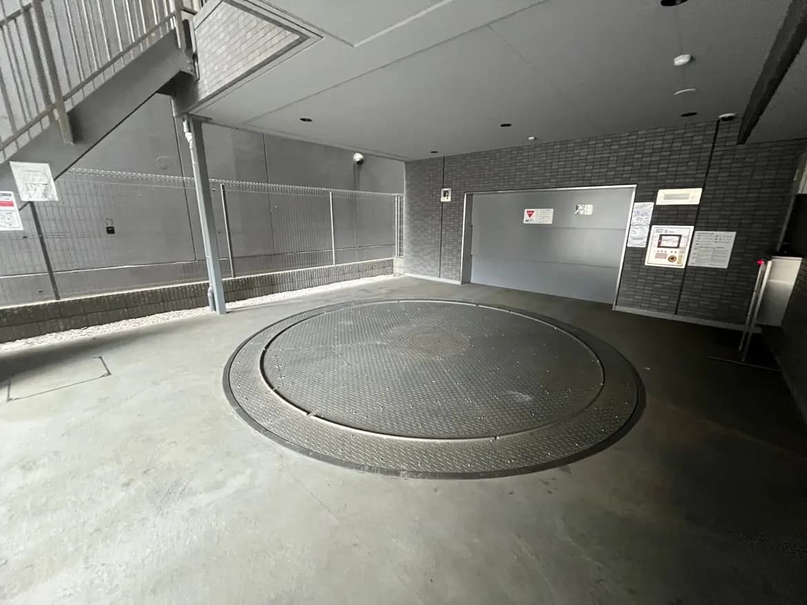 - 地下駐車場の回転式リフトで車両を移動させるための円形プラットフォームと周囲のコンクリート壁、管理案内が掲示されたエリア