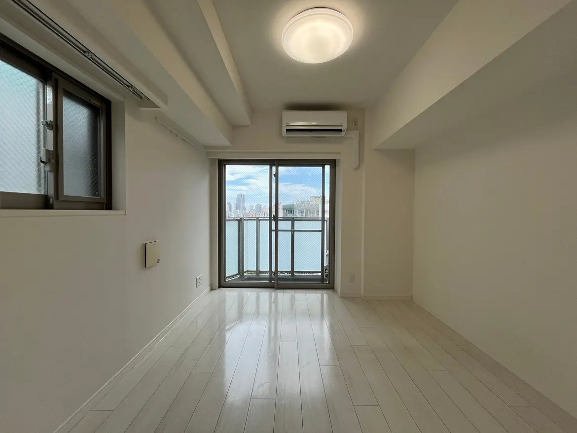 - 明るい色合いのフローリングと大きな窓からの景色が特徴のシンプルな居住スペース、エアコンが設置された部屋の内部