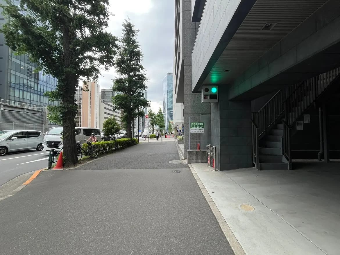 - 都会の歩道に沿った風景、左側に自転車置き場と緑の植栽、背景に高層ビルが立ち並ぶ景観