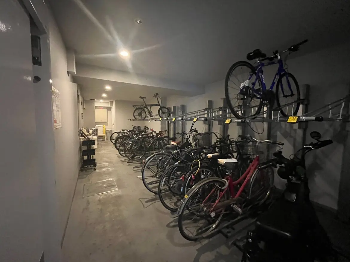 - 自転車が整然と並べられた屋内駐輪場、明るい照明が施された広いスペースと様々な種類の自転車が見える景観