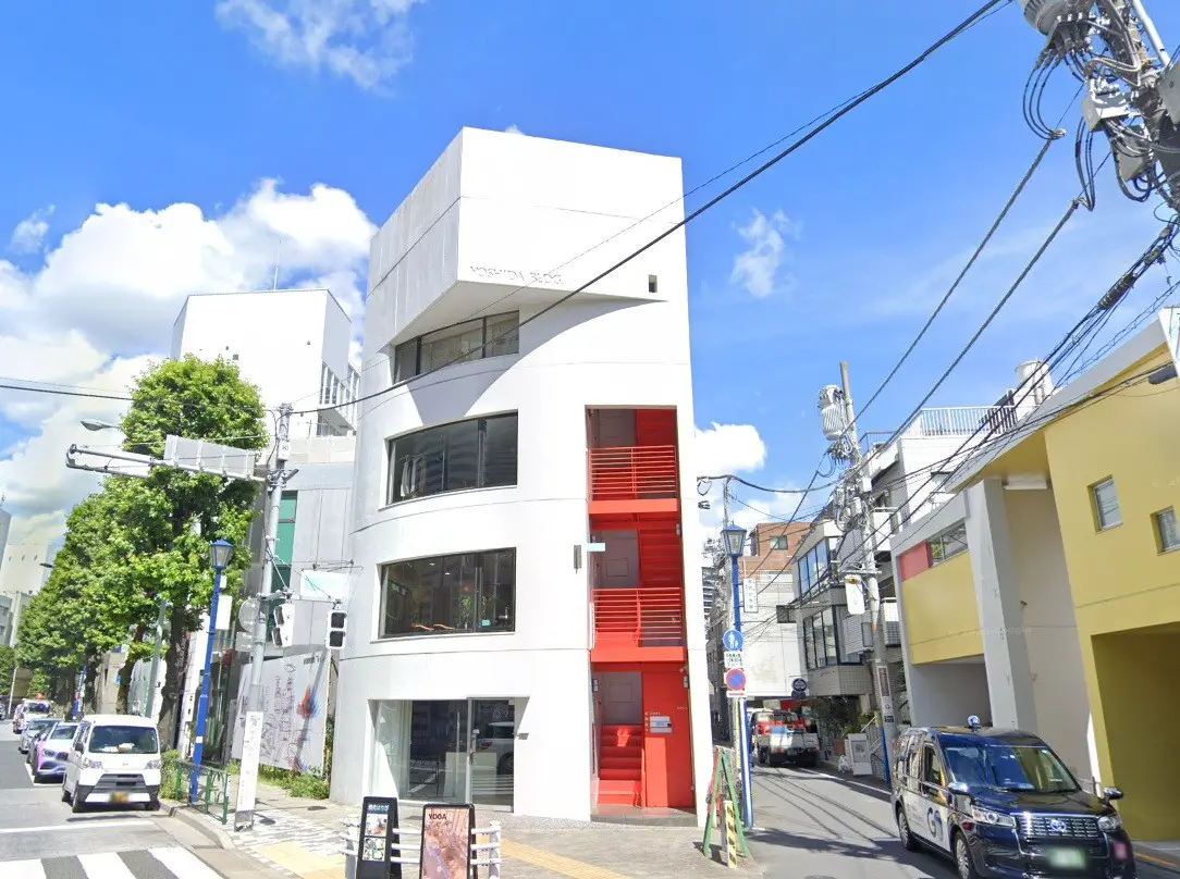 - 白い外壁と赤い階段が特徴的な現代的な建物、周囲には緑豊かな街並みと青空が広がるシーン