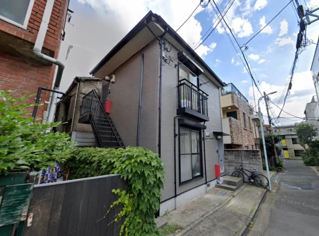- 都会の住宅街にあるモダンな外観の二階建ての家、緑豊かな植栽と階段、周囲の電線が見える風景