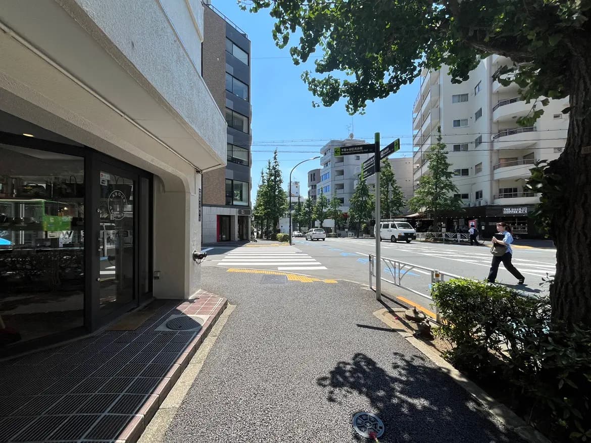 - 明るい青空の下、繁華街の交差点、歩道と店舗の入り口が見える日常の風景