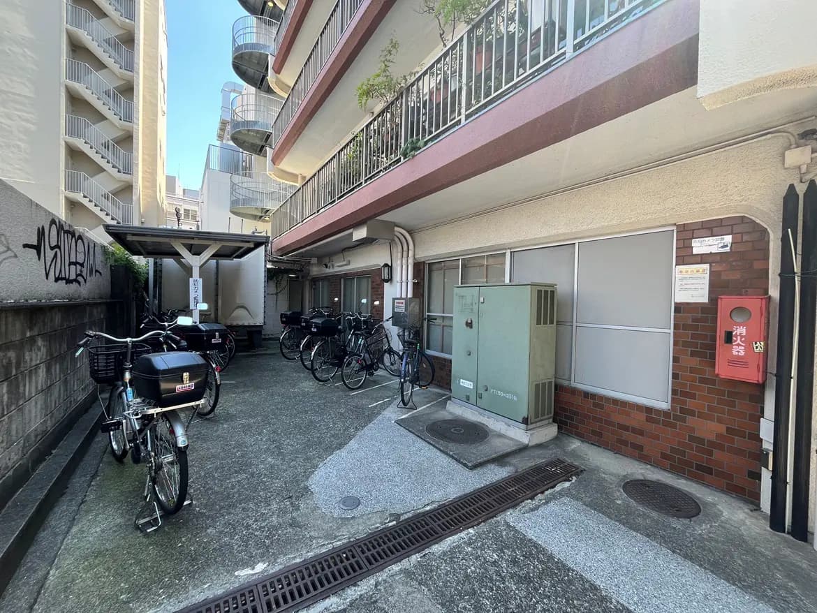- 複数の自転車が停まったアパートの共用スペース、周囲に高層ビルと階段状のバルコニーが見える風景
