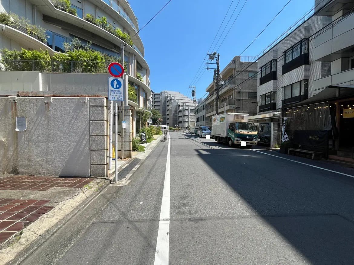 - 明るい青空の下、住宅街の通りの様子、左側には緑がある曲線の建物、交通標識と停車中のトラックが見える風景