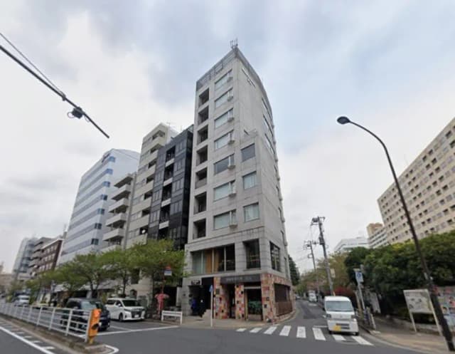 - 都市部に位置するモダンな商業ビル、ガラスの窓とコンクリートの外観、周囲に街路樹と交通信号のある景観