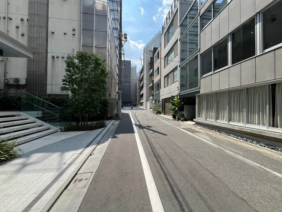 - 近代的なビルが立ち並ぶ都市の街並み、歩道の緑と明るい青空が広がる景色
