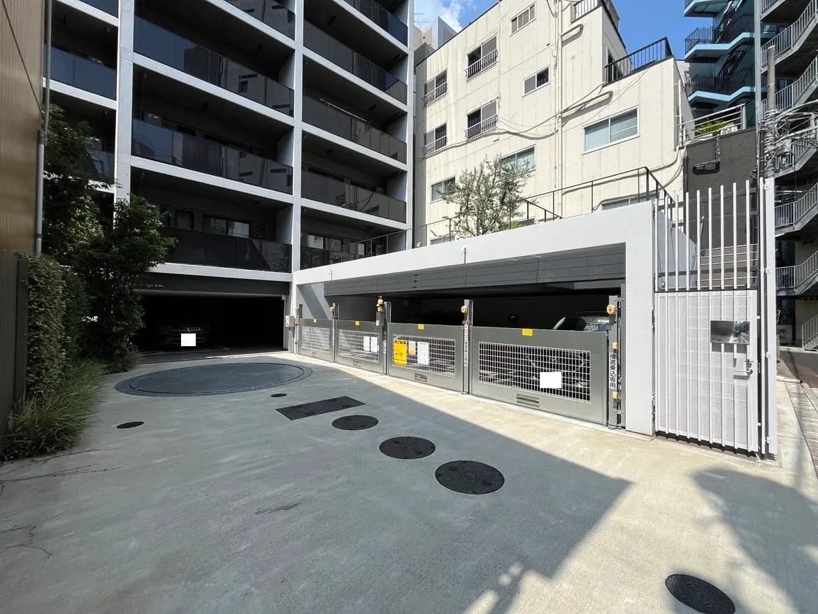 - コンクリート製の駐車場入口、周囲に緑があり、近代的なマンションの外観が見えるシーン
