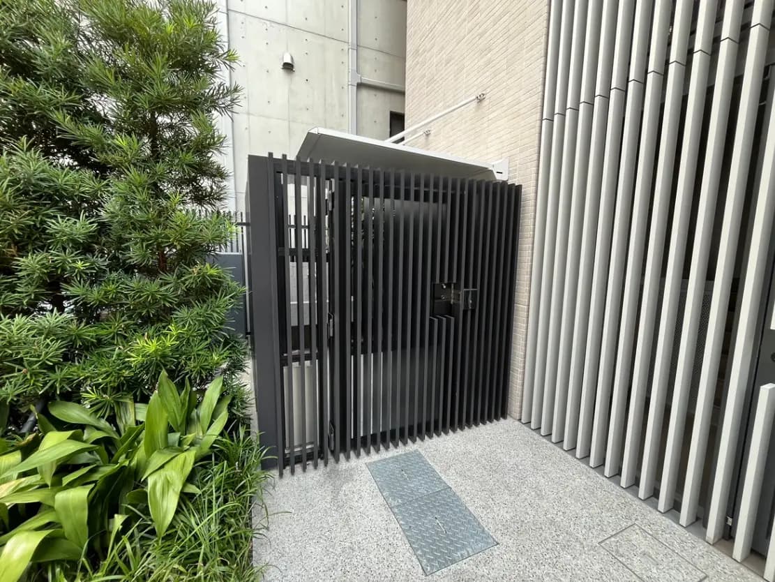 - モダンなデザインの門扉、整然とした植栽と石張りのアプローチ、シンプルな外観を持つ住宅のエントランス