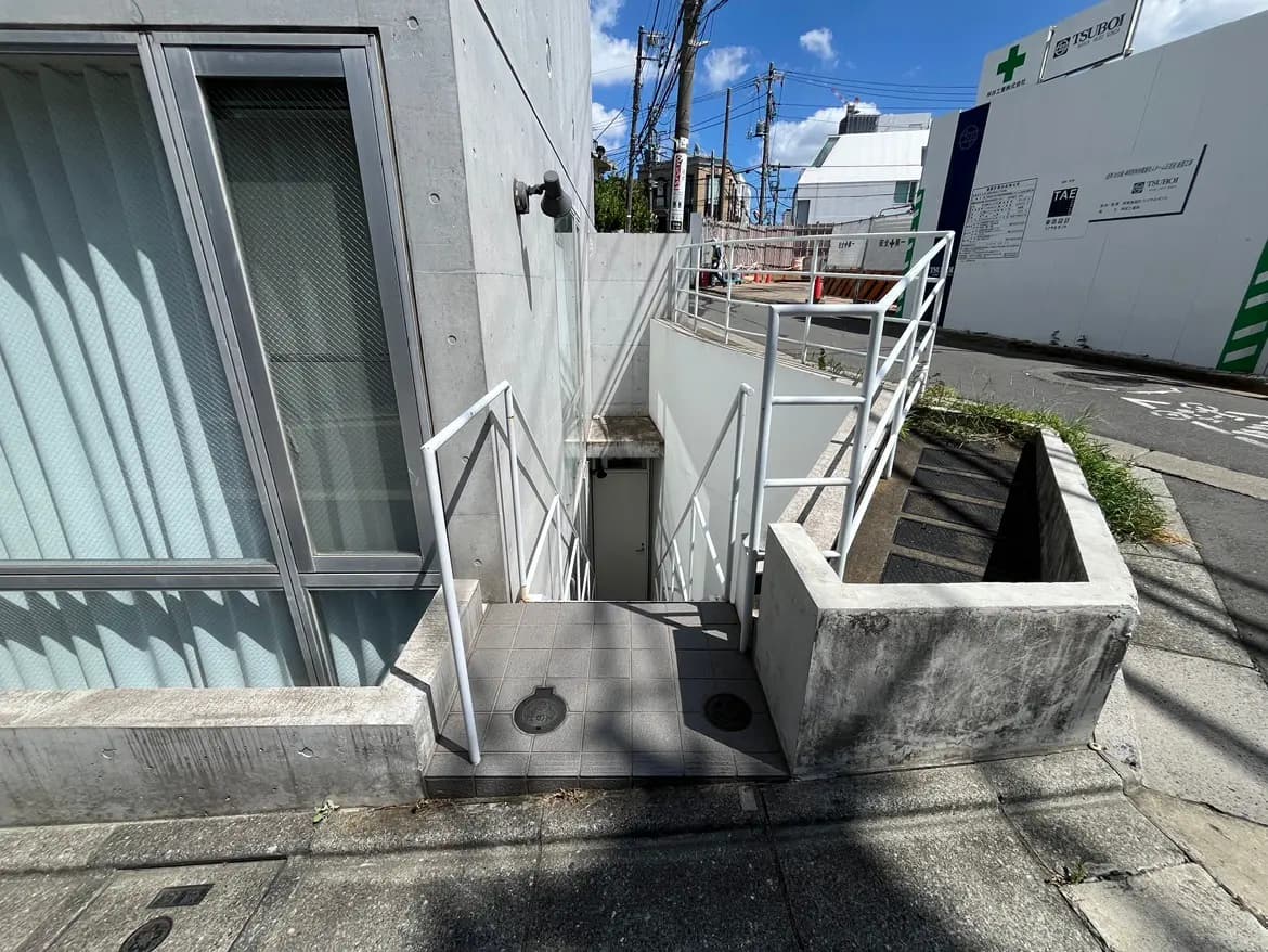 - コンクリート壁のある建物の側面に設置された階段、手すり付きのスロープと明るい青空が広がる風景