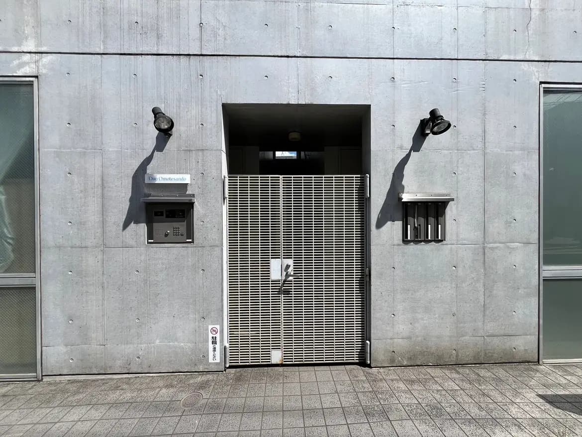 - コンクリート打ちっぱなしの外観と郵便受け、インターホンが設置されたモダンなエントランスの写真