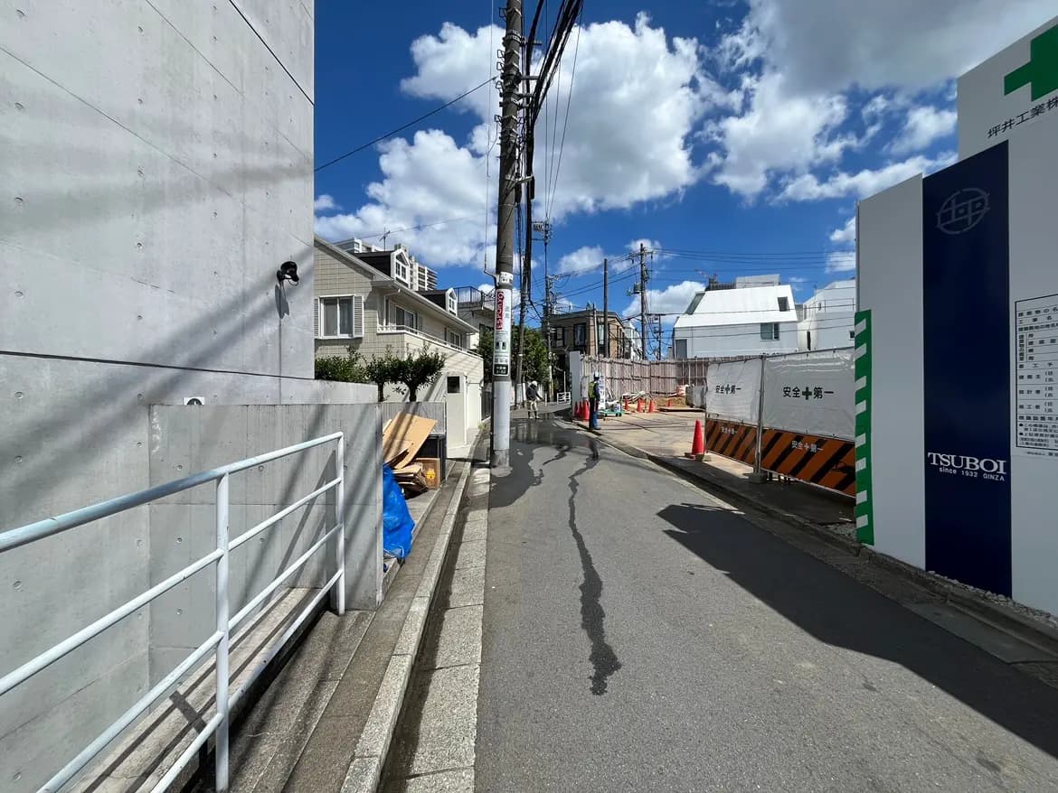 - コンクリート製の壁と青空、周囲に建設現場や住宅が見える街並みの風景