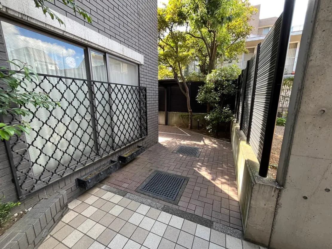 - 煉瓦造りの壁に囲まれた静かな中庭の通路、窓の外には植物が見える明るい風景