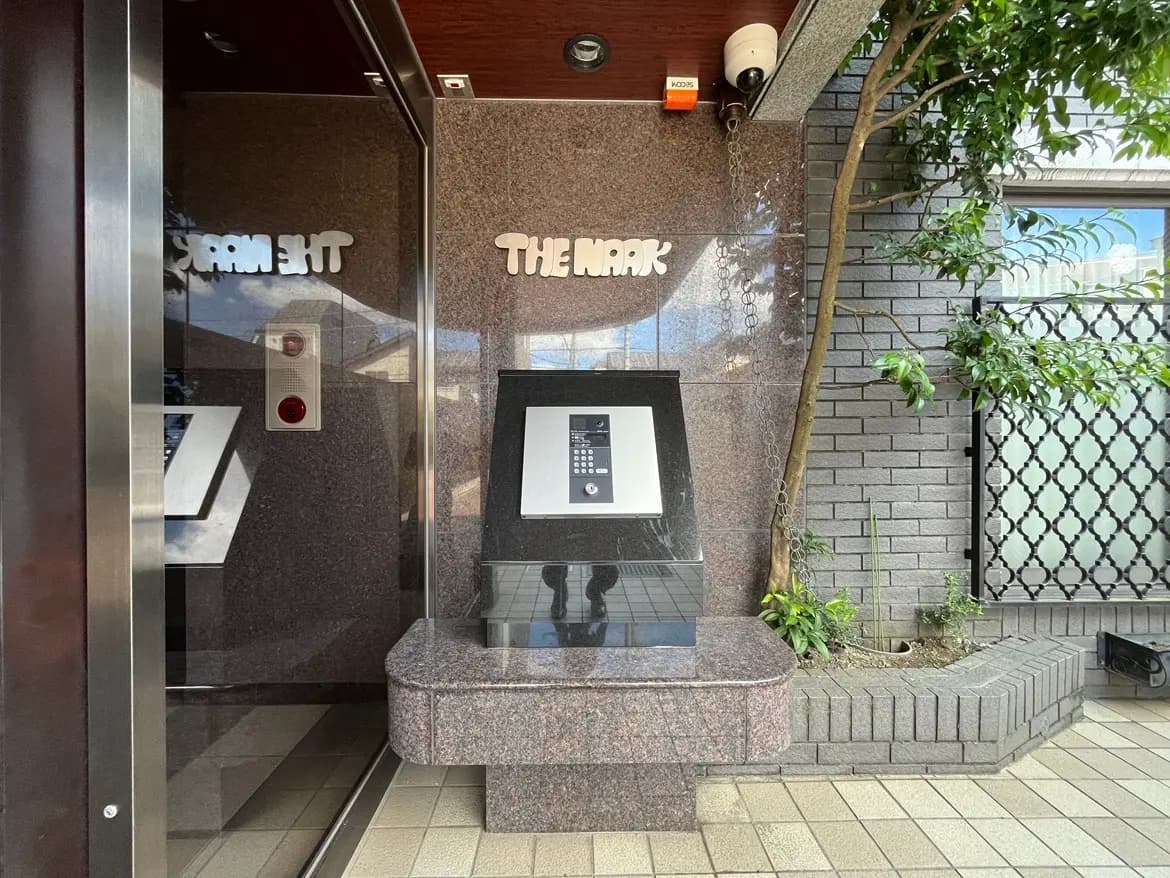 - モダンなエントランスの外観、石造りのパネルとインターホン、周囲には植物が配置されたエントランスデザイン