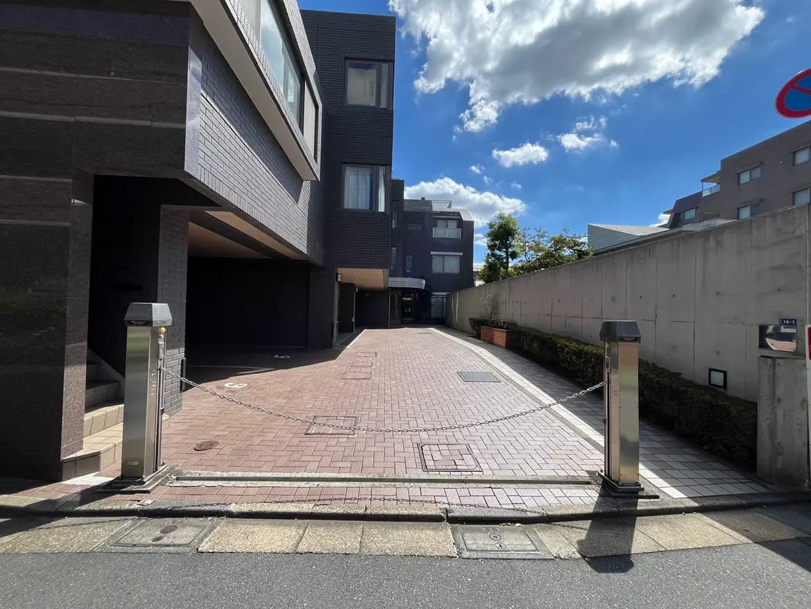 - モダンな外観の建物、整然とした敷地、エントランスのゲートとチェーン、青空と白い雲が広がる景色