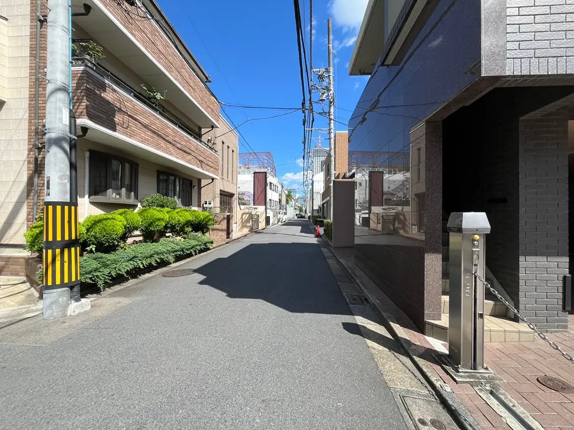 - 静かな住宅街の一本道、両側に植栽が並び、青い空と白い雲が広がる風景