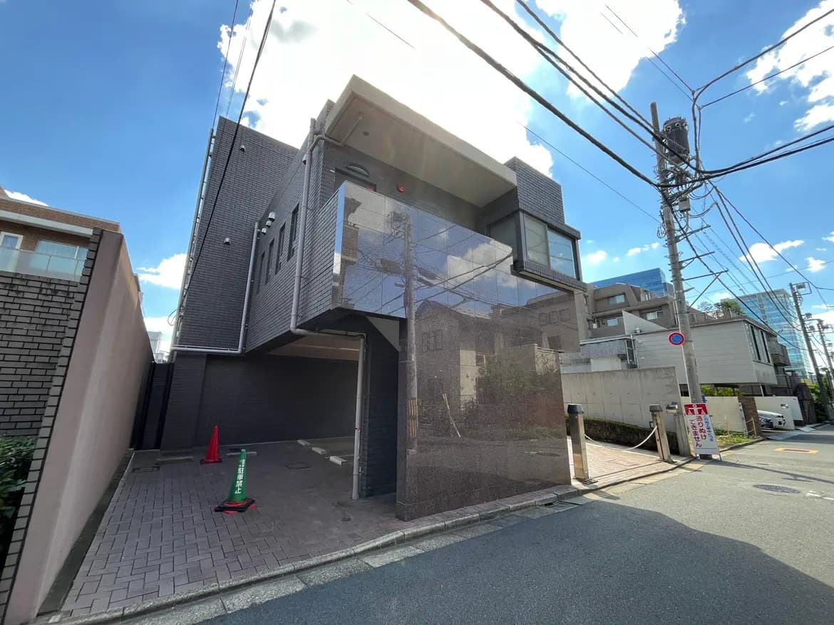 - モダンなデザインの外観を持つ住宅、ガラスバルコニーと洗練されたファサード、青空と電線の景色が広がる通りの風景