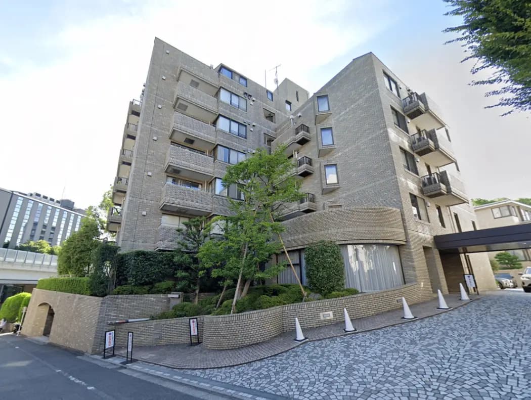- モダンなデザインの集合住宅、グレーの外壁、周囲には緑豊かな植栽と広々とした敷地、エントランスには石畳のアプローチがある風景