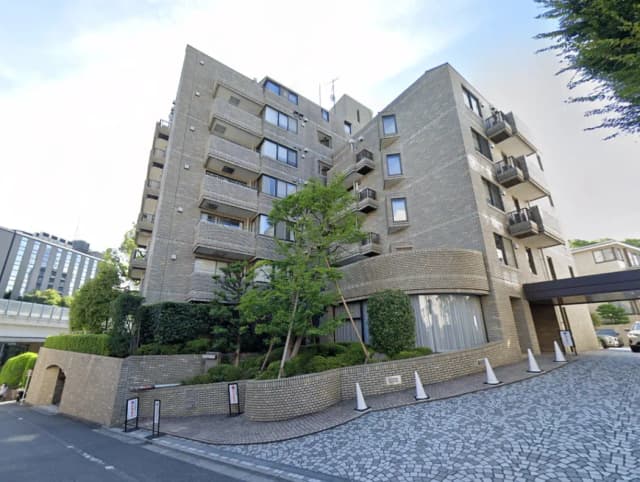 - モダンなデザインの集合住宅、グレーの外壁、周囲には緑豊かな植栽と広々とした敷地、エントランスには石畳のアプローチがある風景