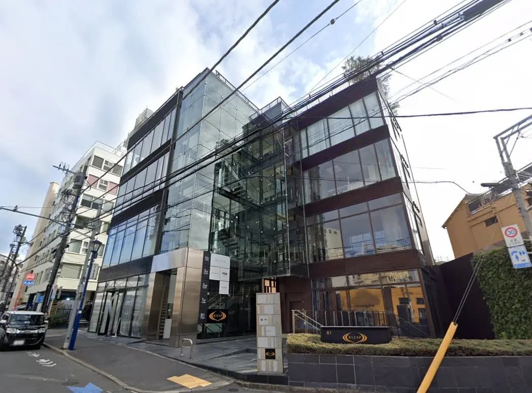 - 近代的なガラス張りのオフィスビル、エントランスとその周辺の建物が見える風景、周囲に電線が走る街並み