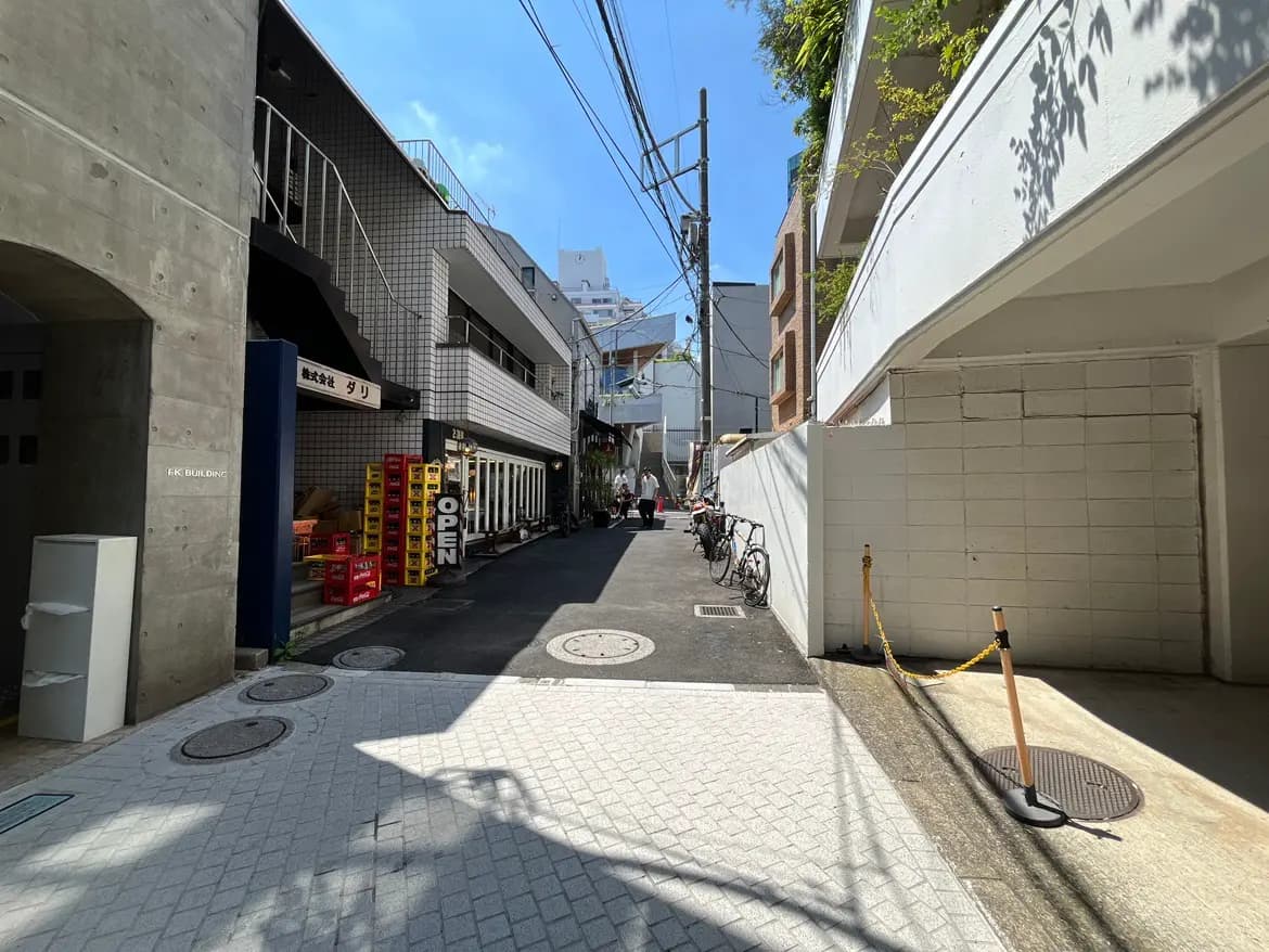- 都会の裏道、店舗や飲食店が並ぶ通り、青空に映える建物と自転車が停車している風景