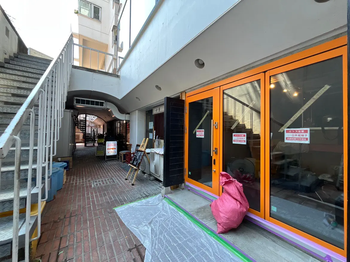 - 鮮やいオレンジの扉が特徴的な商業施設のエントランス、階段と看板が並ぶアーケード通りの風景