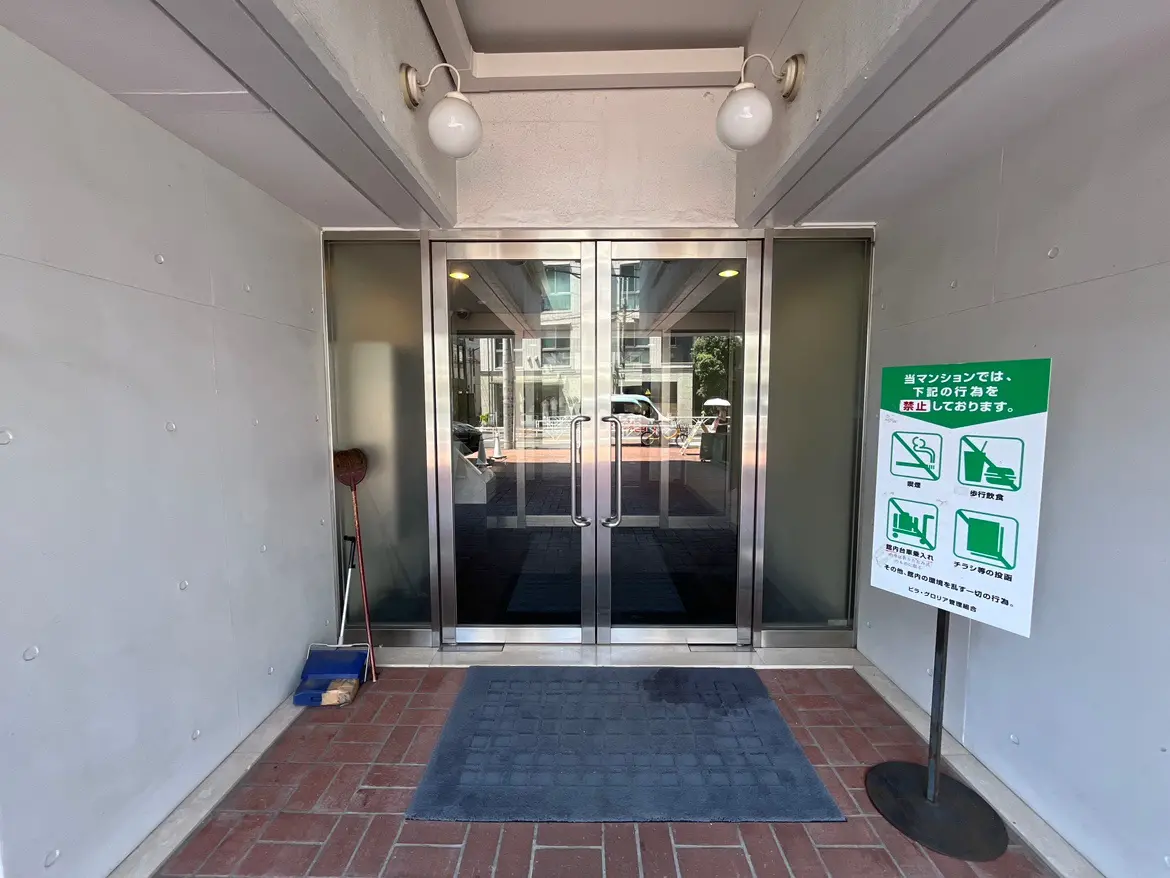- モダンなマンションのエントランス、ガラス扉とブロックタイルの床、注意事項の掲示板が設置された入り口