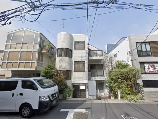 - 白いタイル張りの現代的なマンション外観、隣接するガラス張りの建物と自然豊かな植栽、街中の風景
