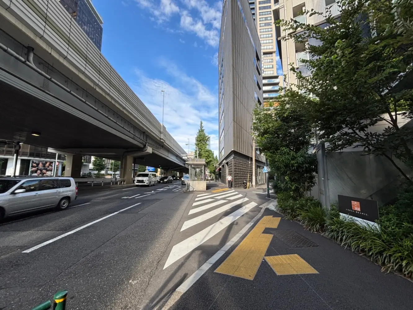 - 高速道路の下に広がる都市の風景、青空と近代的なビル群、通行する車と交差点の横断歩道の様子