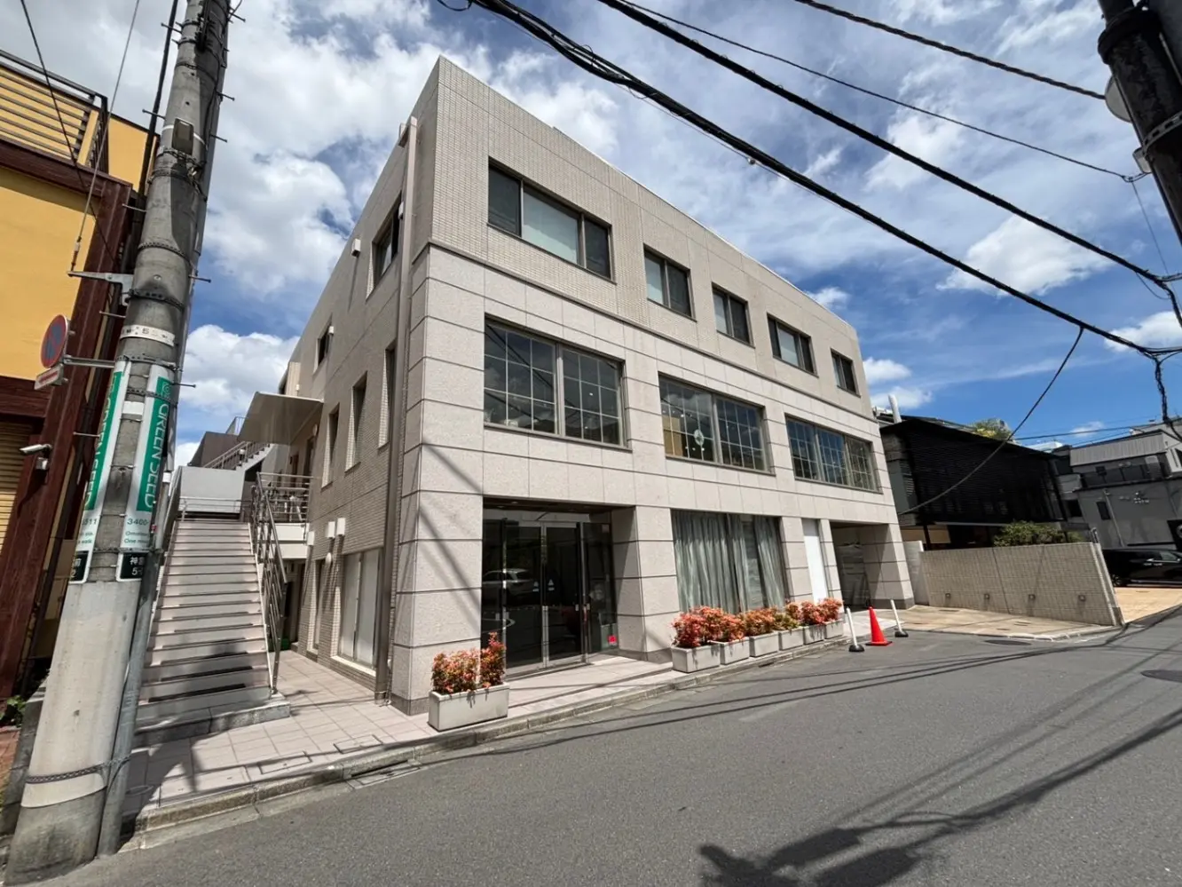 - モダンな外観のビル、白いタイル張りのデザイン、建物の前に階段と植え込み、青空が広がる街並み