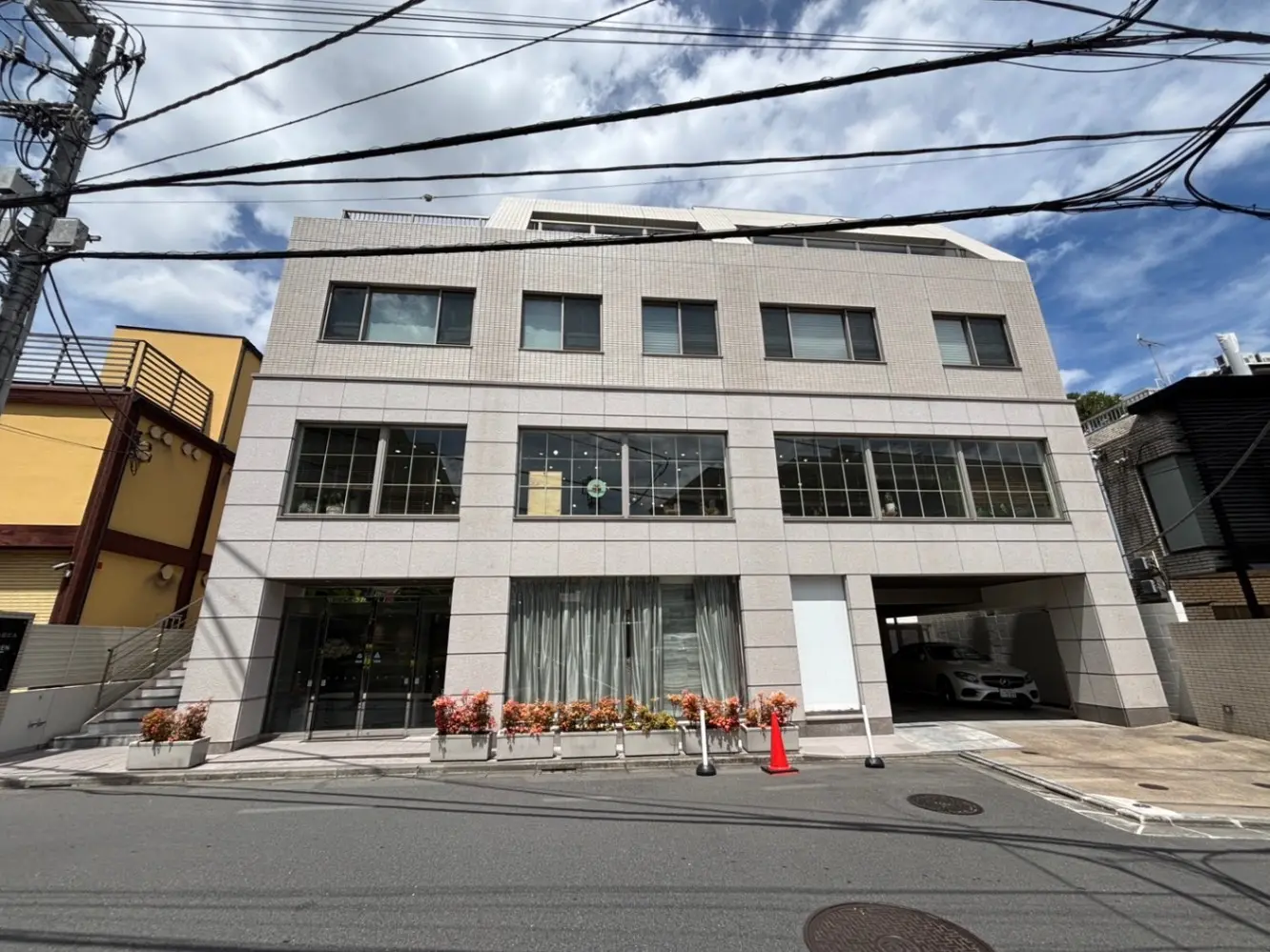 - モダンな外観のテナントビル、2階建て、広い窓とグレーのタイル張り、周囲に植栽と電柱のある街並み