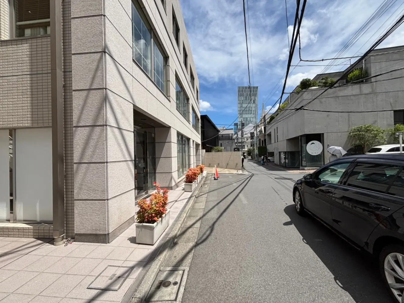 - コンクリートとガラスの現代的な建物が立ち並ぶ通り、プランターに彩られた景観と青空が見える街並み