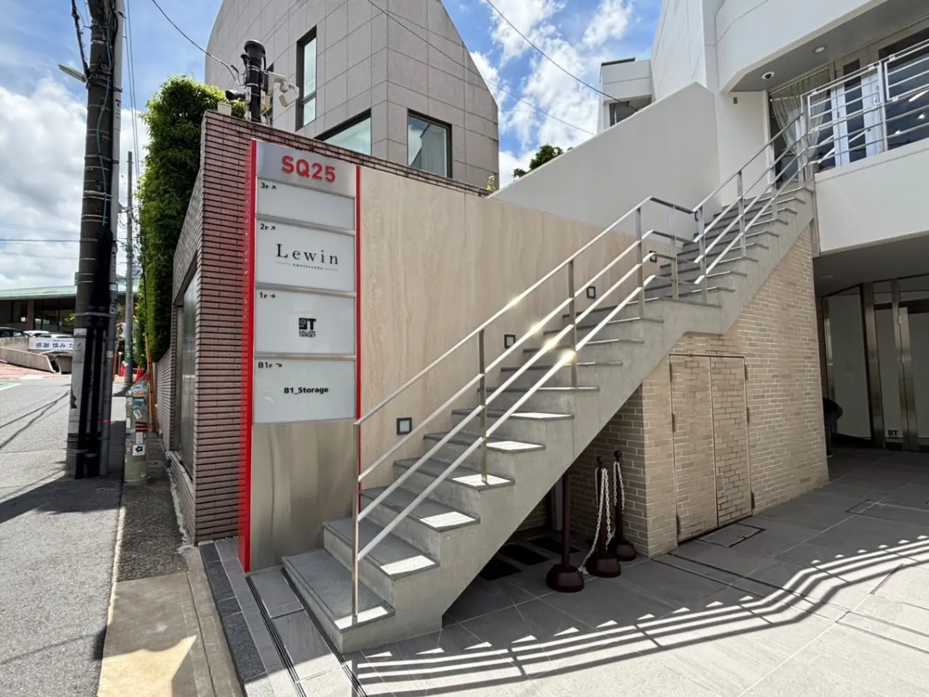 - 現代的な建物の入り口、階段と案内板があり、周囲には緑が植えられたエントランスデザイン