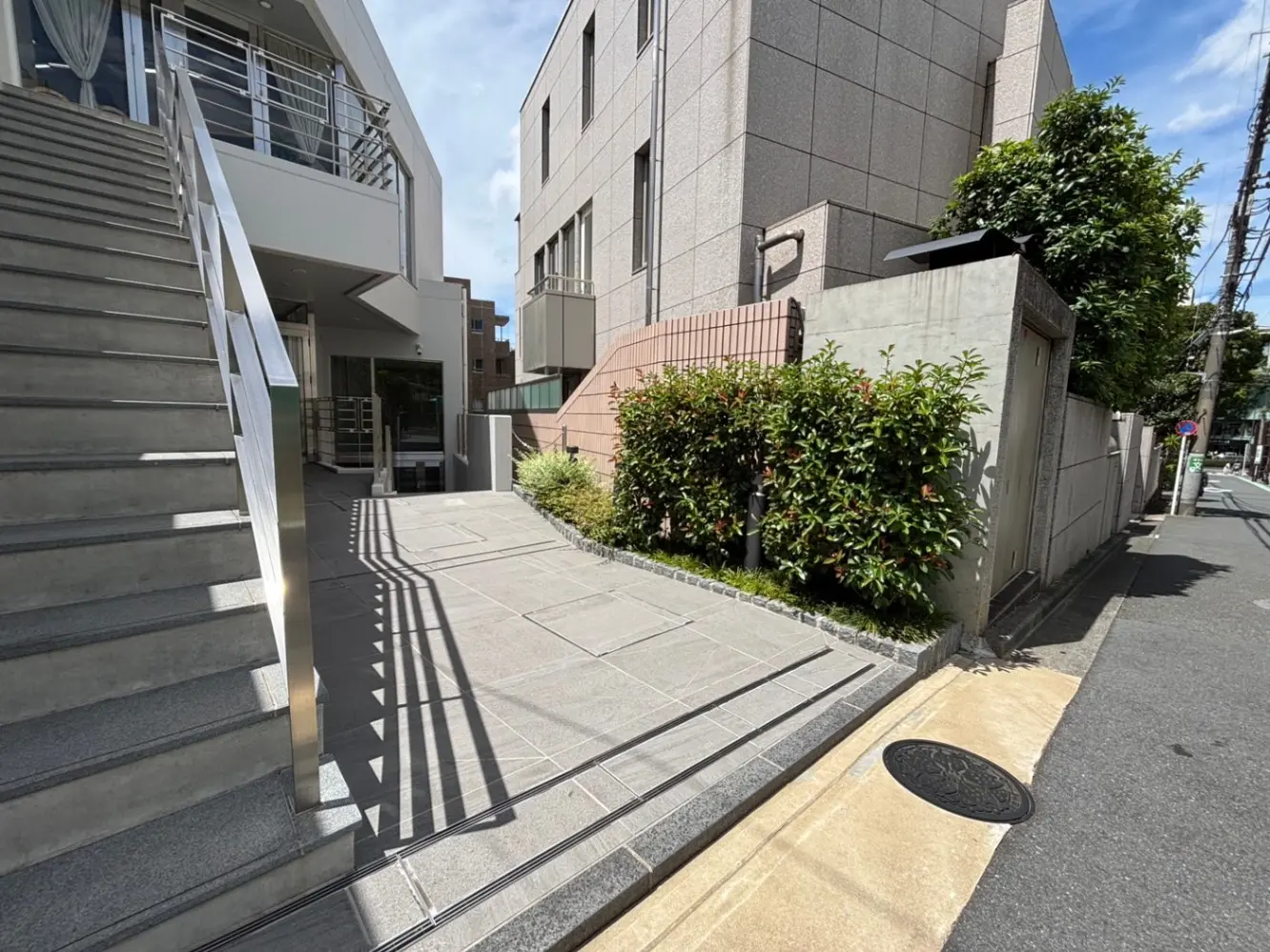- 階段とガラスの手すりがあるモダンなエントランス、植栽が施された庭と舗装されたアプローチパス