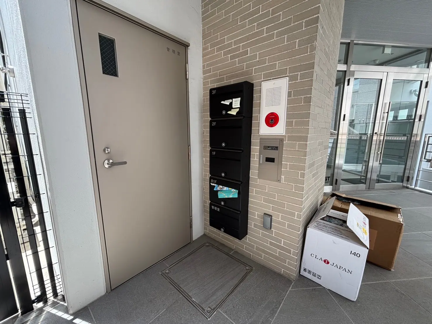 - モダンなマンションのエントランス、郵便受けとインターホンが設置された壁、荷物が置かれた玄関口の風景