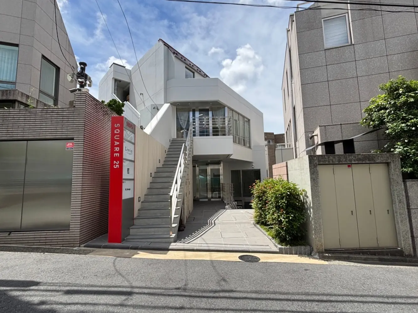 - モダンなデザインの建物「SQUARE 25」、階段とガラス張りのエントランス、周囲に緑がある風景