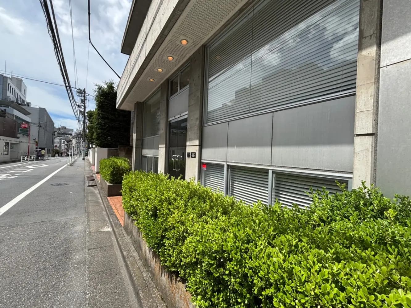 - 近代的な建物の外観、整えられた植栽と舗装された歩道、青空の下での街角の風景
