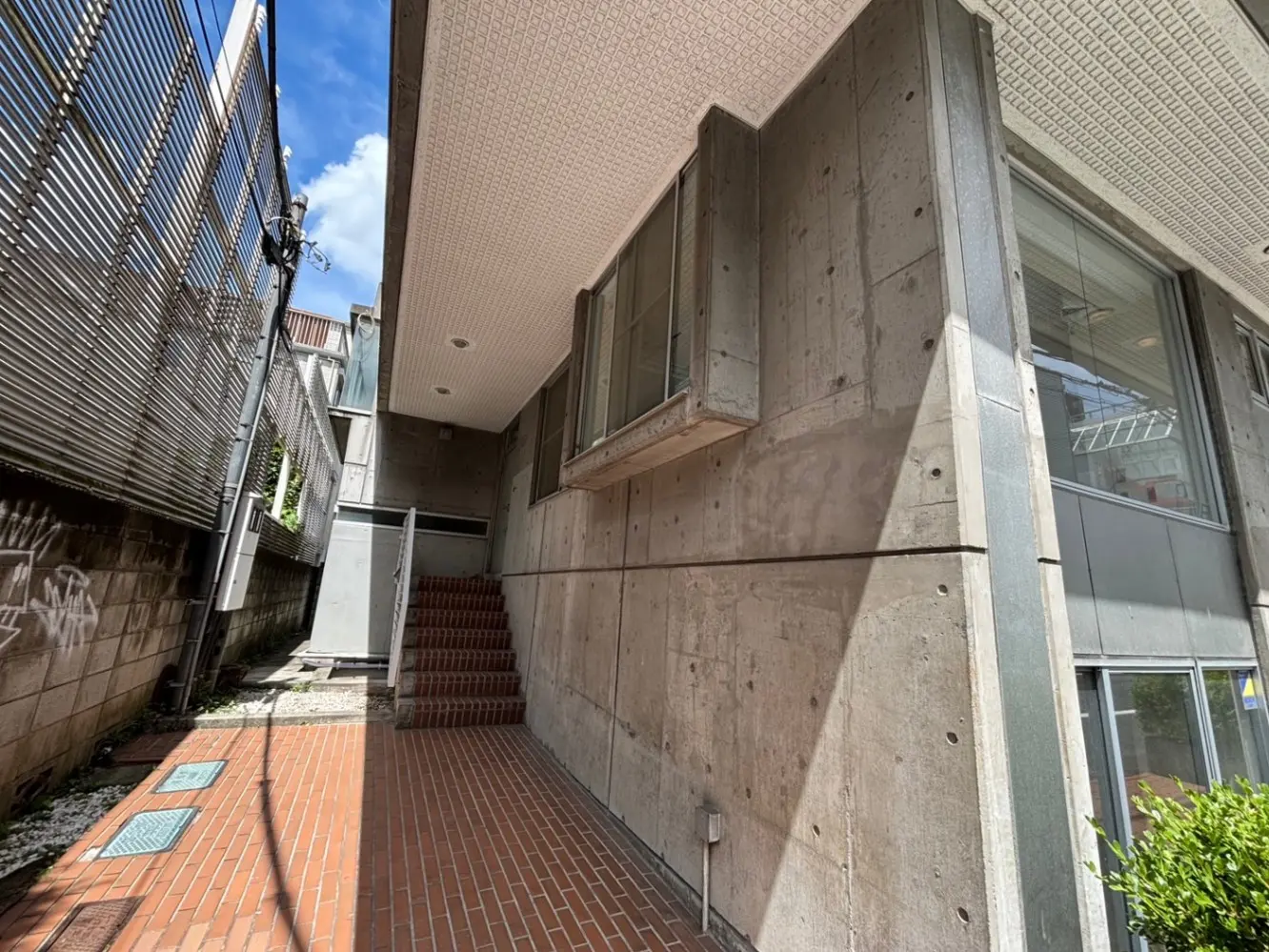 - 現代的なコンクリート構造の建物の側面と、赤煉瓦の通路、階段がある明るい入り口の風景