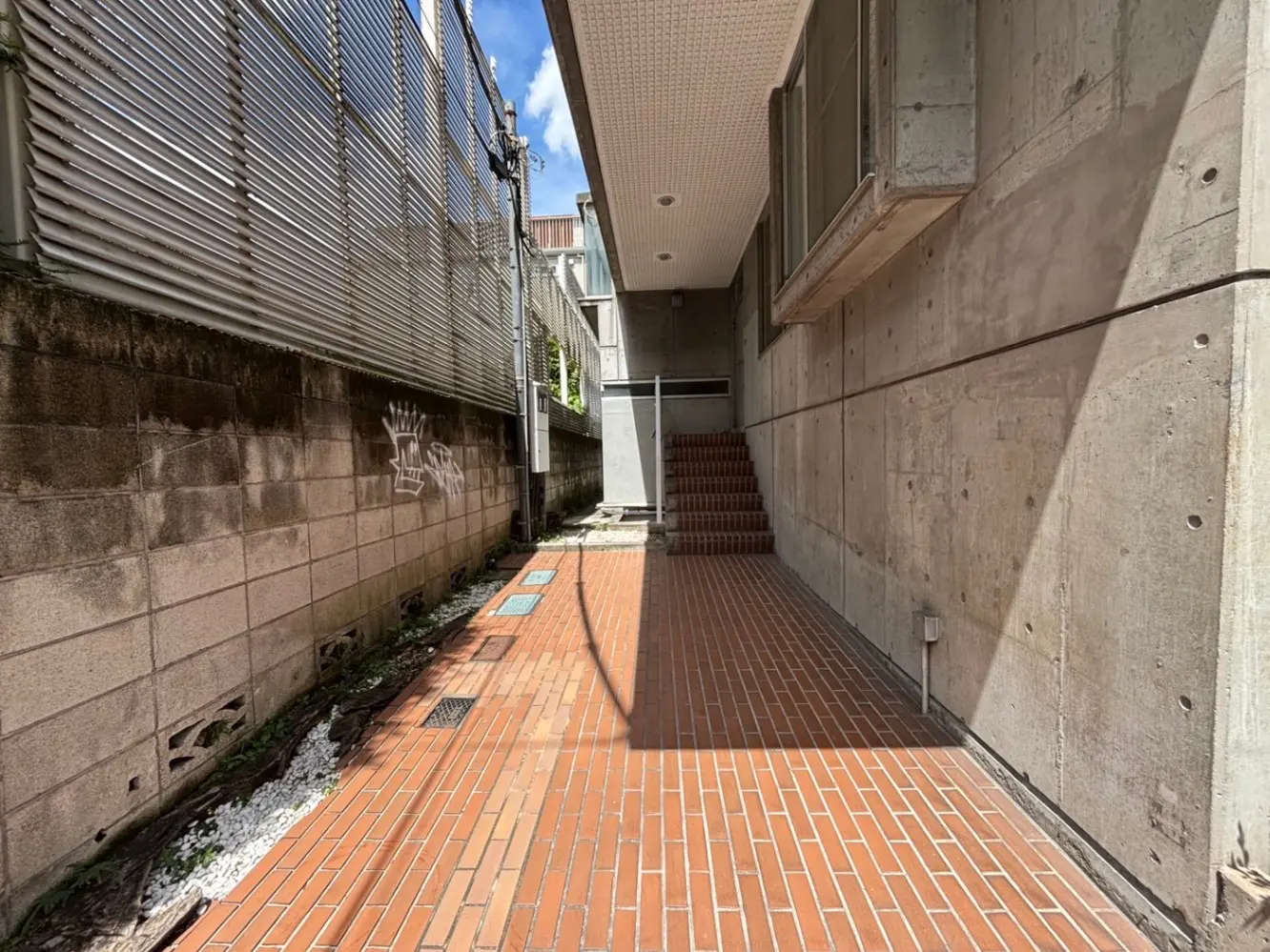 - コンクリートの壁に囲まれた通路、レンガの床と側面にはグラフィティ、日差しが差し込む静かな空間