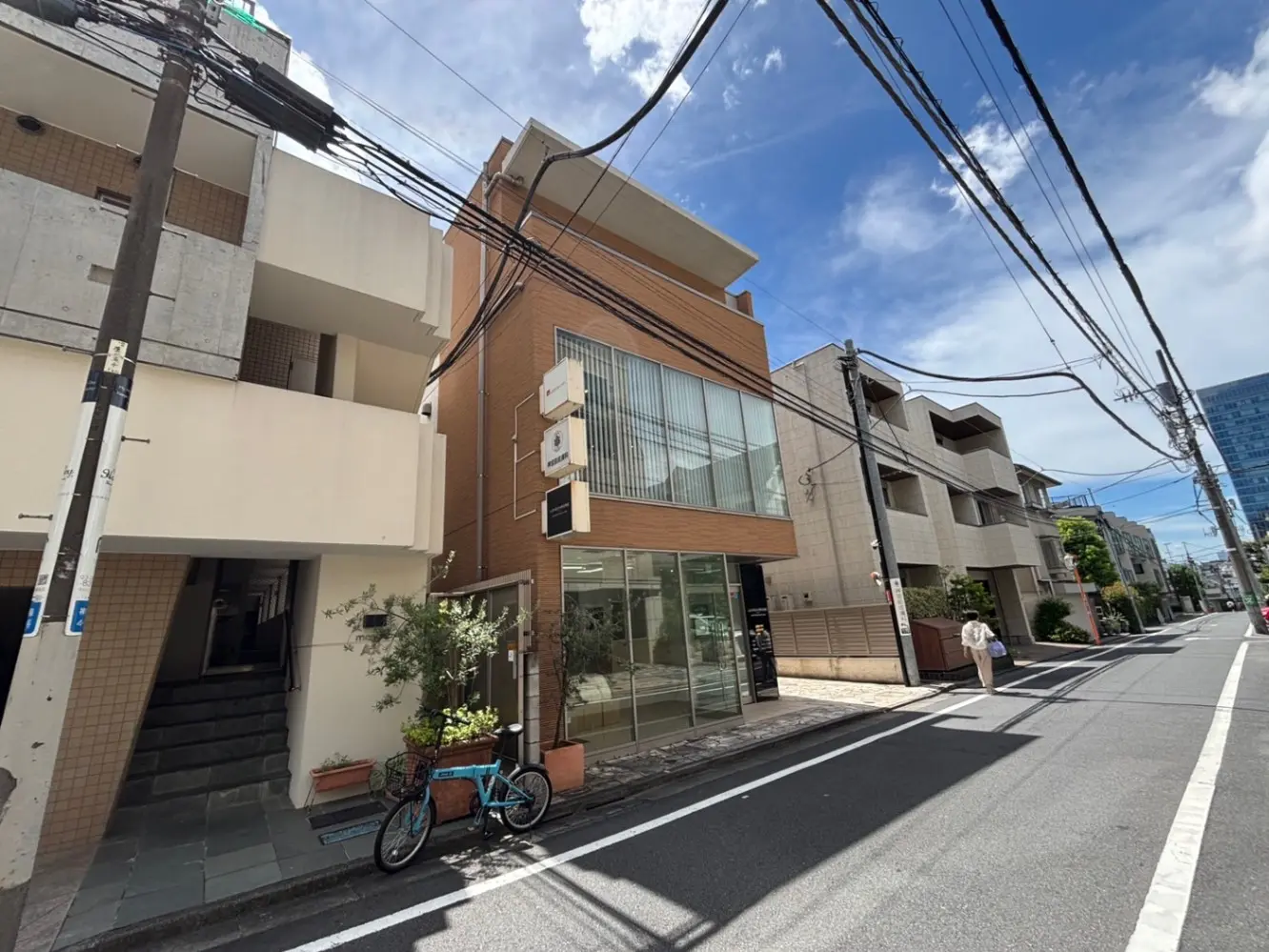 - 商業ビルの外観、近代的なデザインの建物と周囲の住宅街、青空と電線が交錯する街並み
