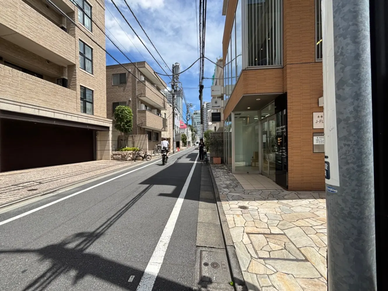 - 都会の街並み、近代的なビルと住宅、舗装された歩道に自転車が通る光景、青空の下のシーン