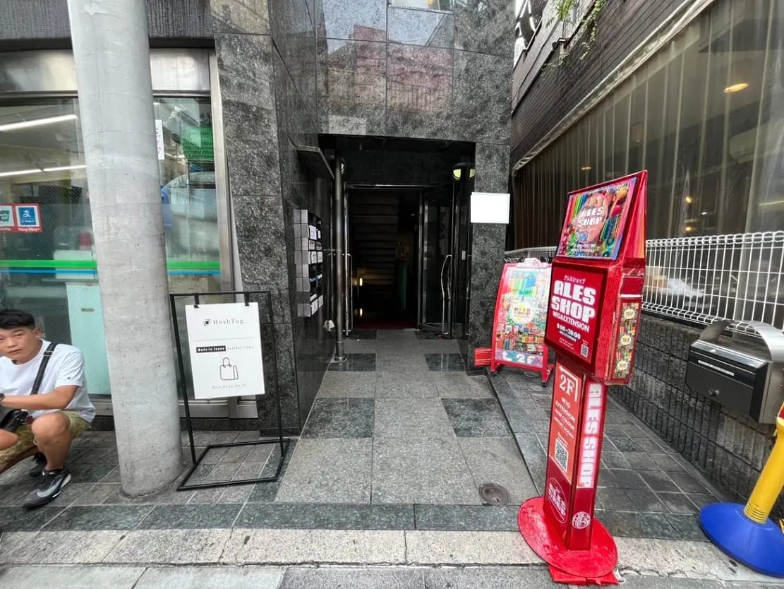 - 石造りのビルの入り口、店舗案内板と遊技機が並ぶ様子、周囲に都市の雰囲気が漂う景観